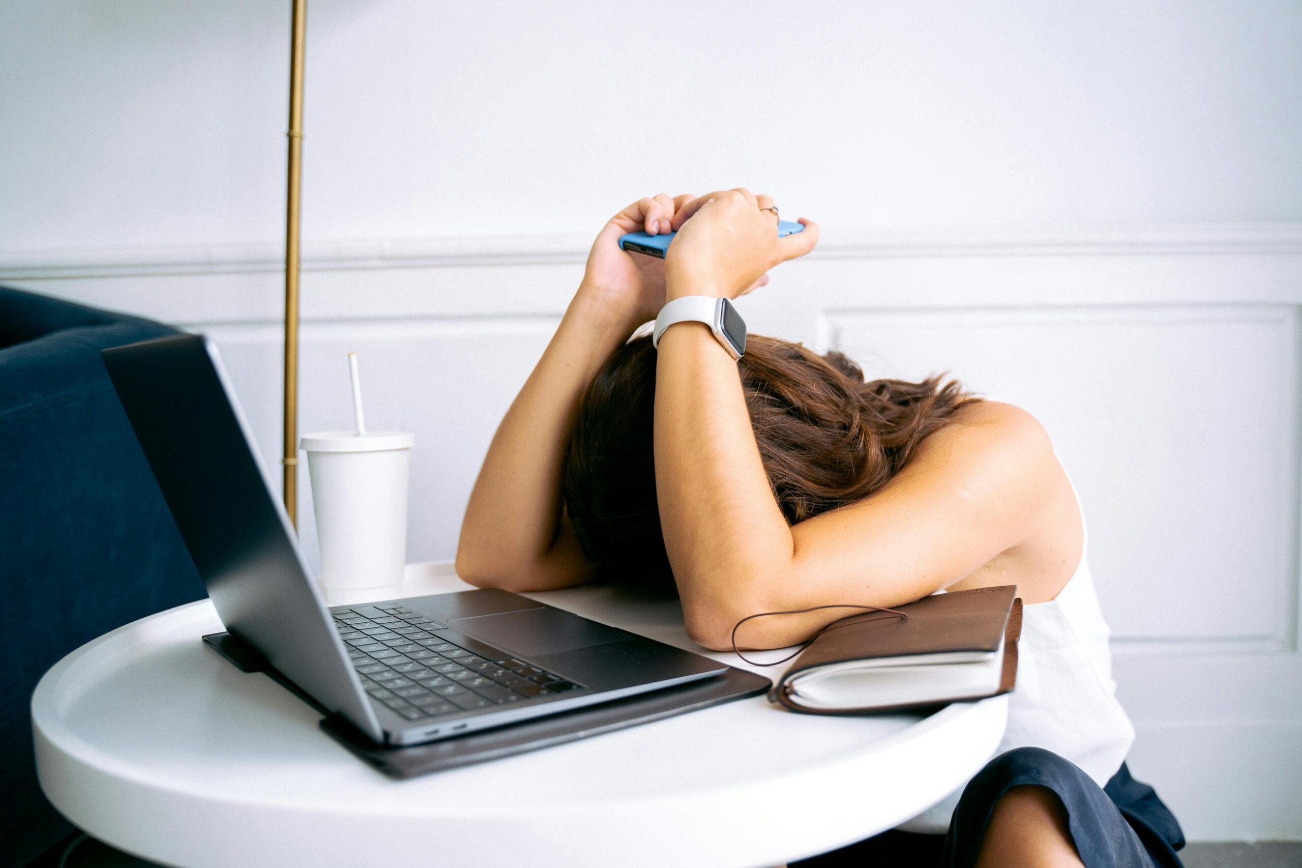 Frustrated wellness practitioner surrounded by papers and laptop, struggling with tech overwhelm
